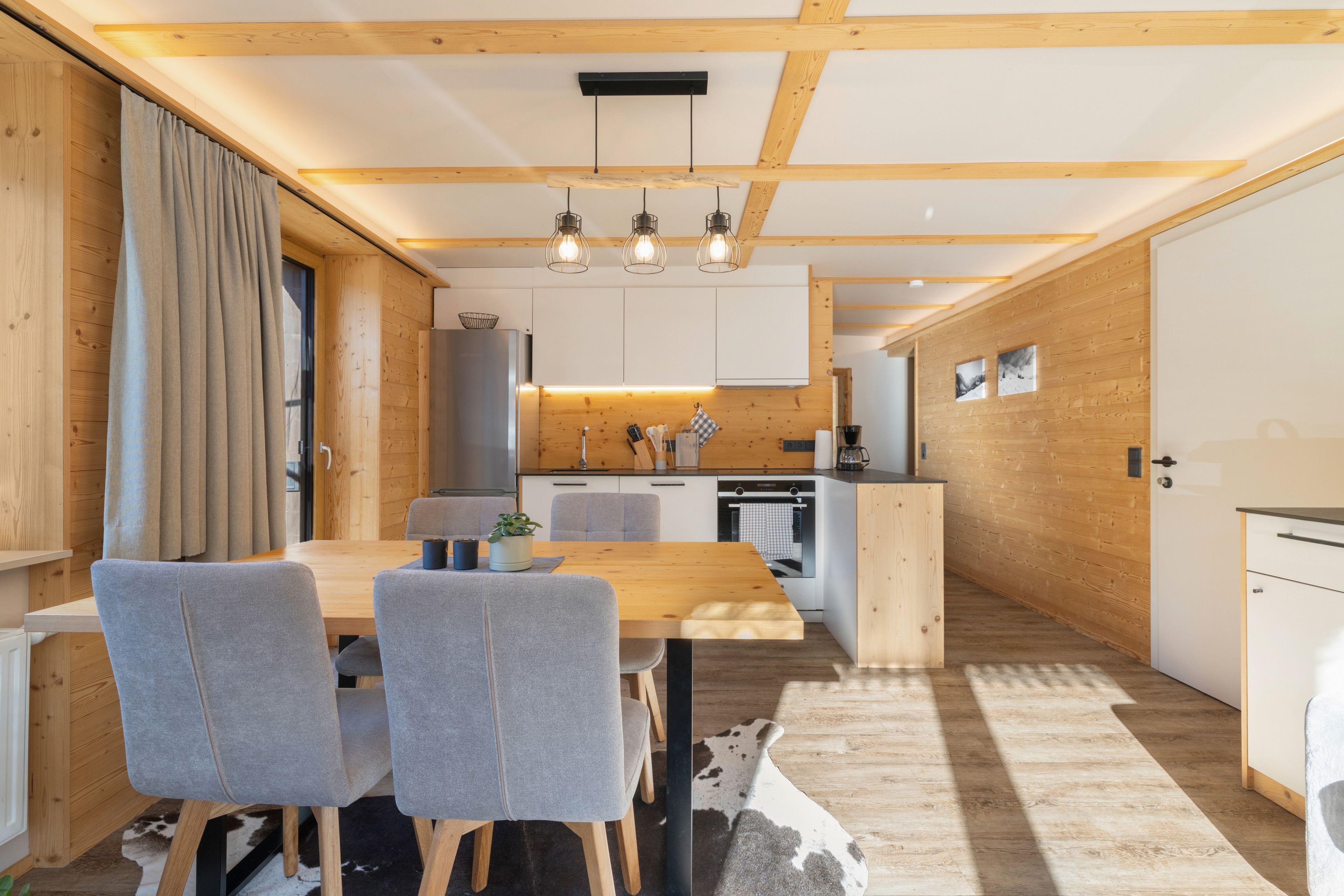 A modern kitchen with wooden beams, a dining area with grey chairs, and a central island.