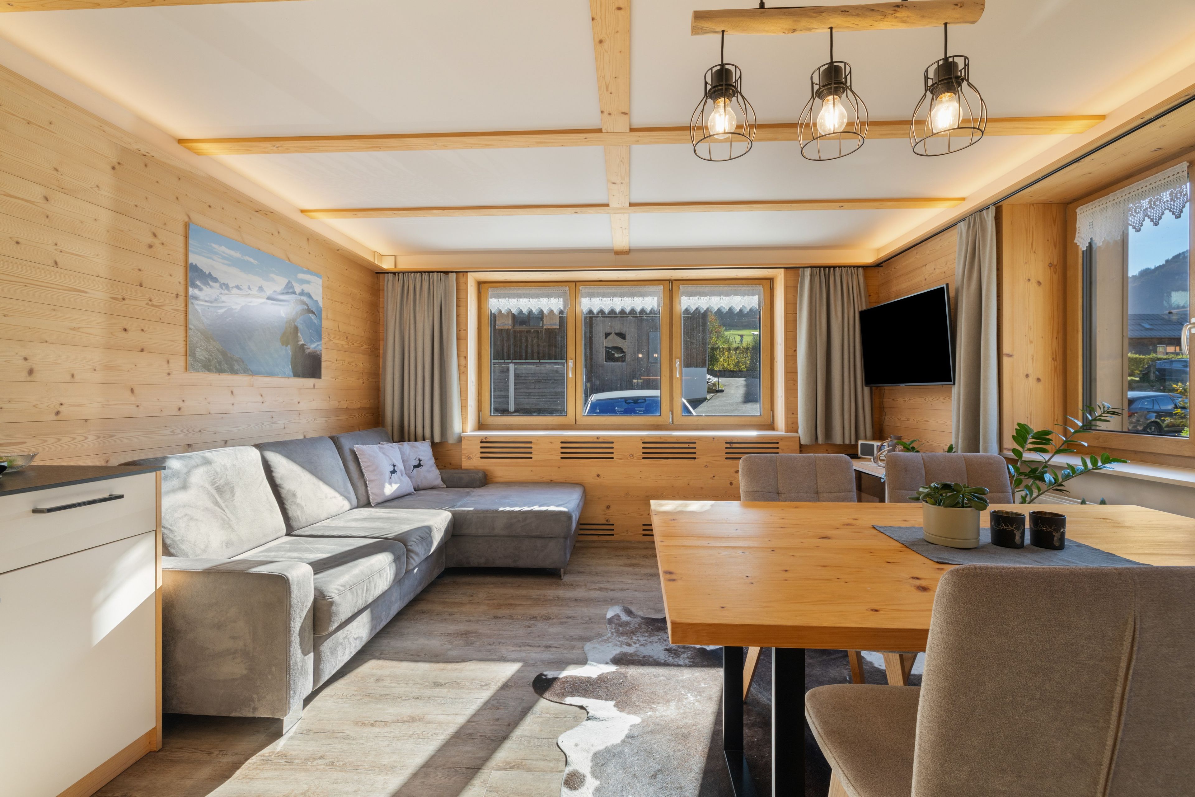 A modern interior with a wooden ceiling, a sofa, a dining table, and a large window.