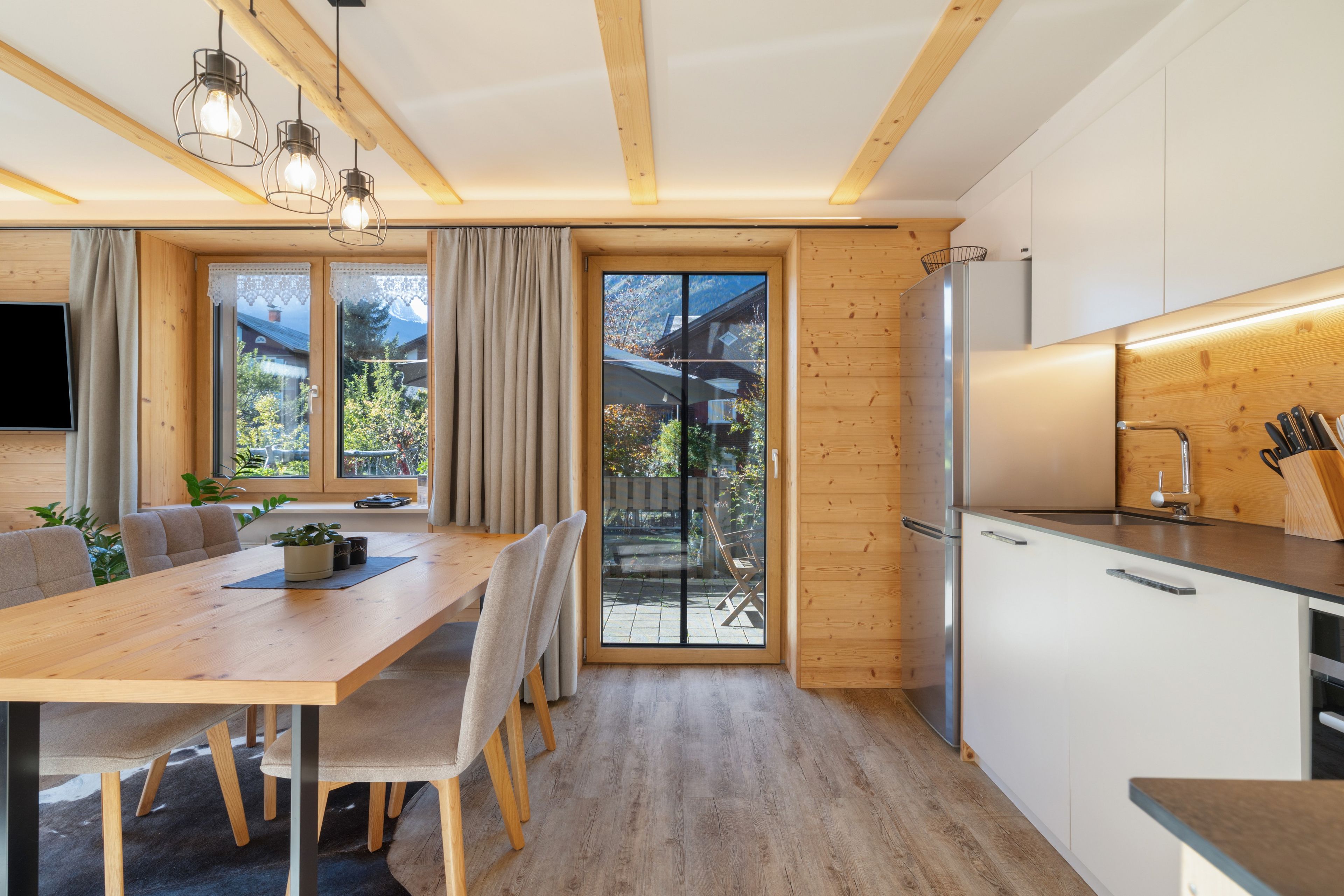 Une cuisine moderne avec des meubles en bois, un réfrigérateur en acier inoxydable et un coin repas comprenant une table et des chaises en bois.