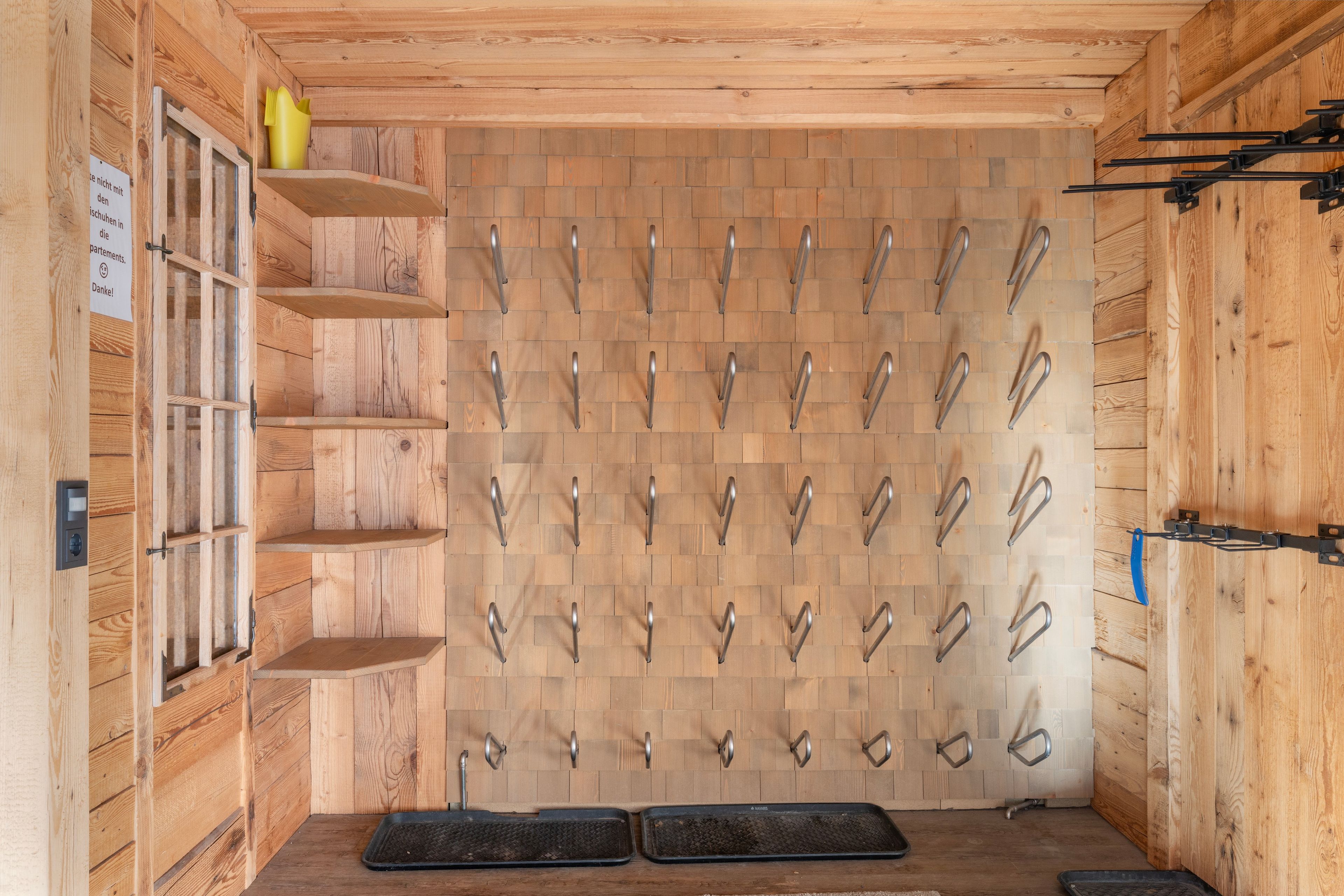 Una habitación con paredes de madera, varios ganchos para colgar objetos y una puerta con un cartel.