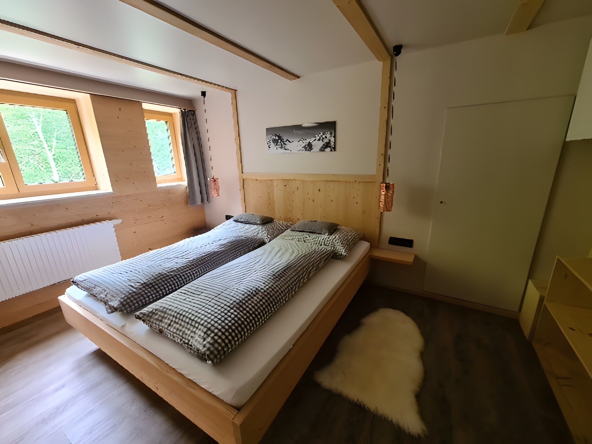 Una habitación con cama, ventana, puerta y un cuadro en la pared.