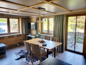 A dining area with a wooden table, chairs, and a cowhide rug. There is a television on the wall and a view of the outdoors through large windows. - Apartment 'Wohnung "Steinbock"' with Mountain View, Private Terrace and Wi-Fi (Au)