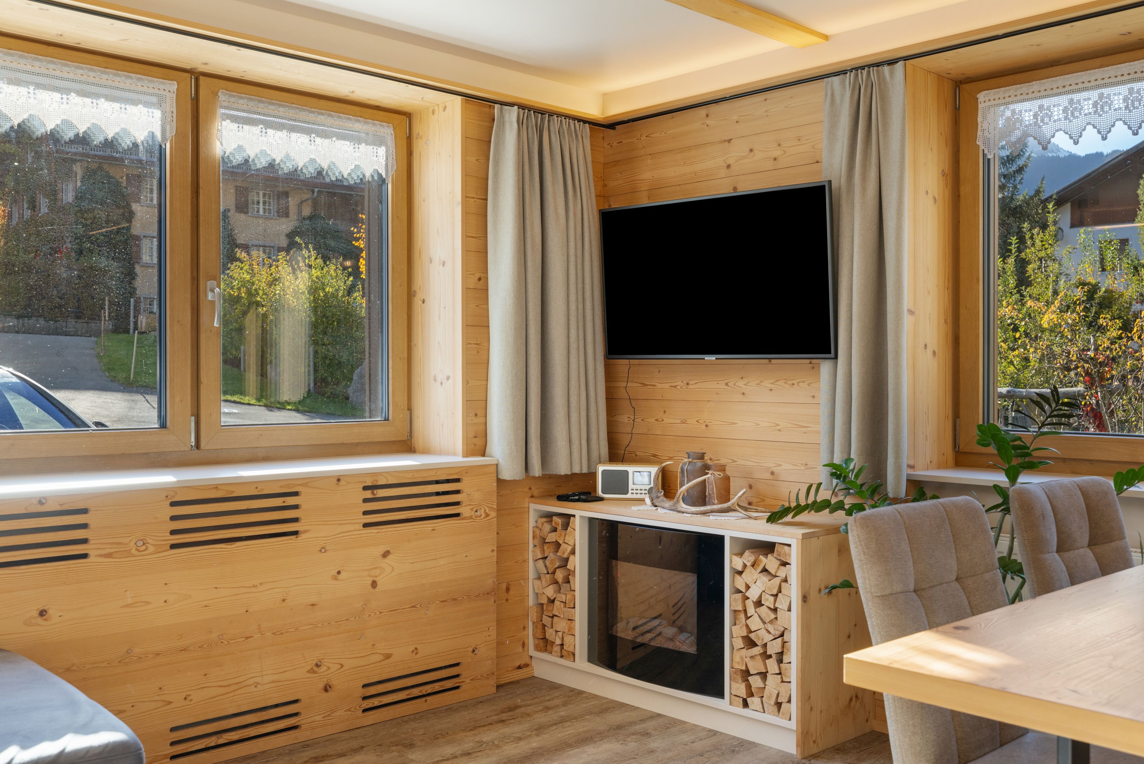 A cozy cabin interior with a large window, a television, a small table, and a seating area.