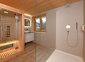 A modern bathroom with a wooden vanity, a built-in heater, a shower with a handheld hose, and a window providing natural light.