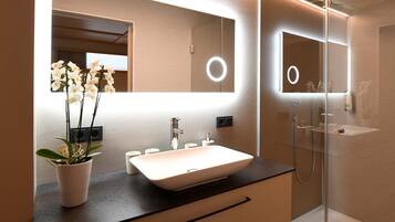 A modern bathroom with a large mirror, a white sink, and a potted orchid.
