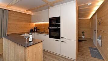 Een moderne keuken met houten wanden, een inbouwoven en een bar met een wijnfles en glazen.