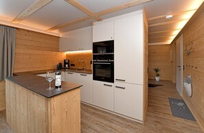 Ett modernt kök med träpanel på väggarna, en inbyggd ugn och en bardisk med en vinflaska och glas.