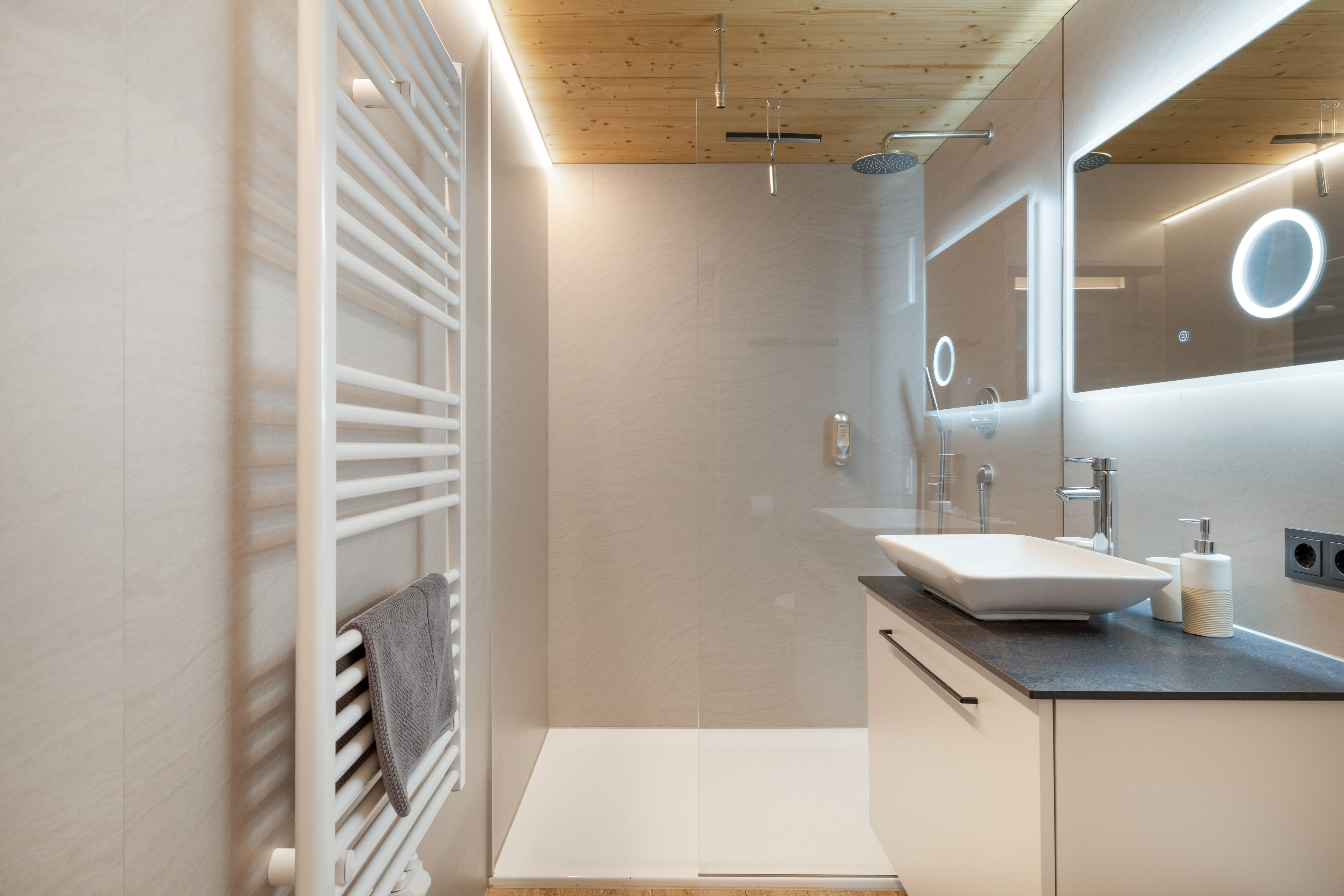Une salle de bain moderne dotée d’une douche intégrée, d’un grand miroir et d’un meuble-lavabo avec un évier.