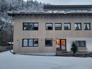 A modern two-story building with a flat roof, multiple windows, and a small entrance with steps.
