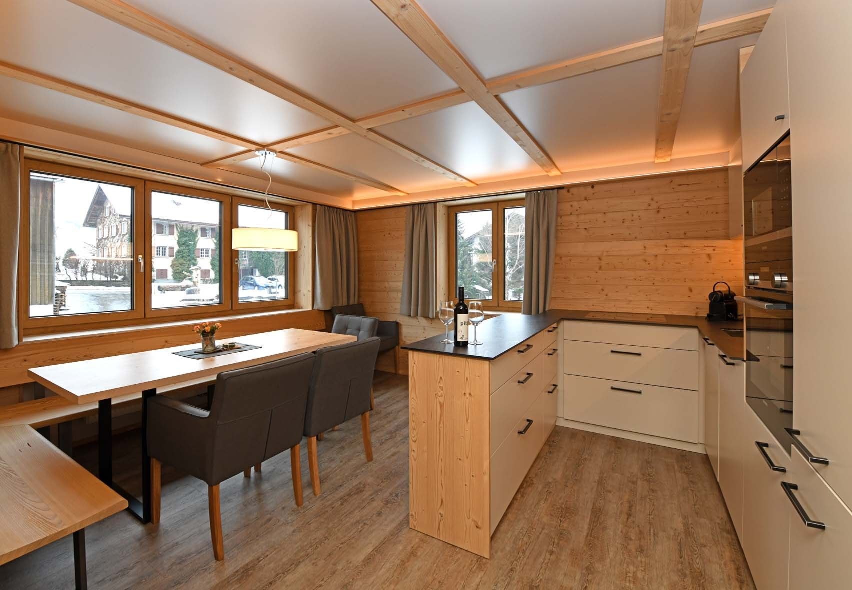Een moderne keuken met houten kastjes, een eethoek met een tafel en stoelen, en grote ramen met uitzicht.
