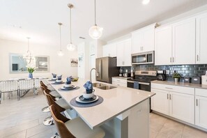 A modern kitchen with white cabinets, stainless steel appliances, and pendant lighting. - Charming 4BR Home w/ Pool Mickey & Star Wars! (Kissimmee)