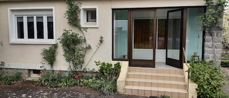 Une maison avec un toit en tuiles, une porte d’entrée avec des panneaux de verre et un petit jardin.