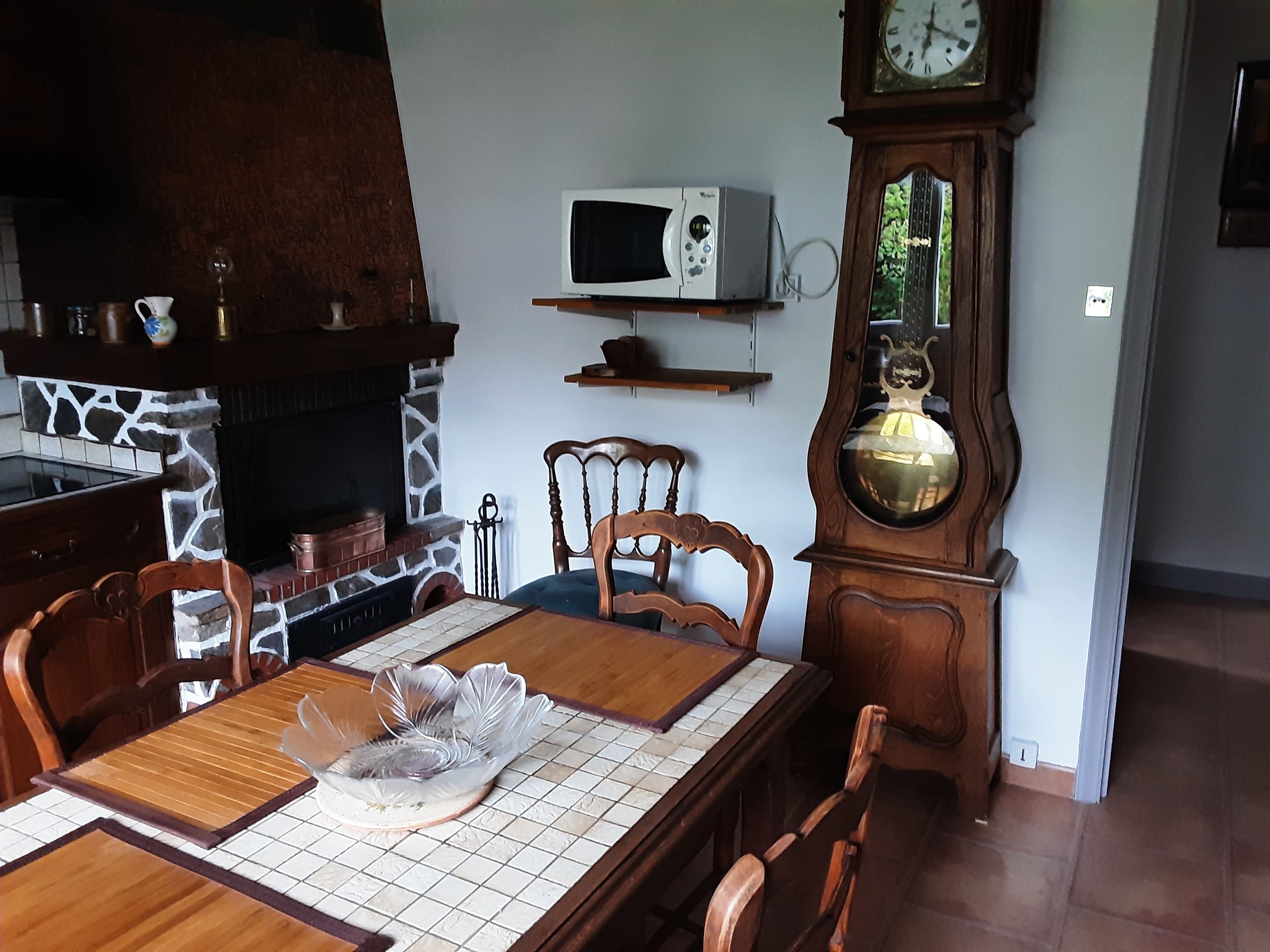 Een eetgedeelte met een houten tafel, stoelen, een klok, een magnetron en een open haard.