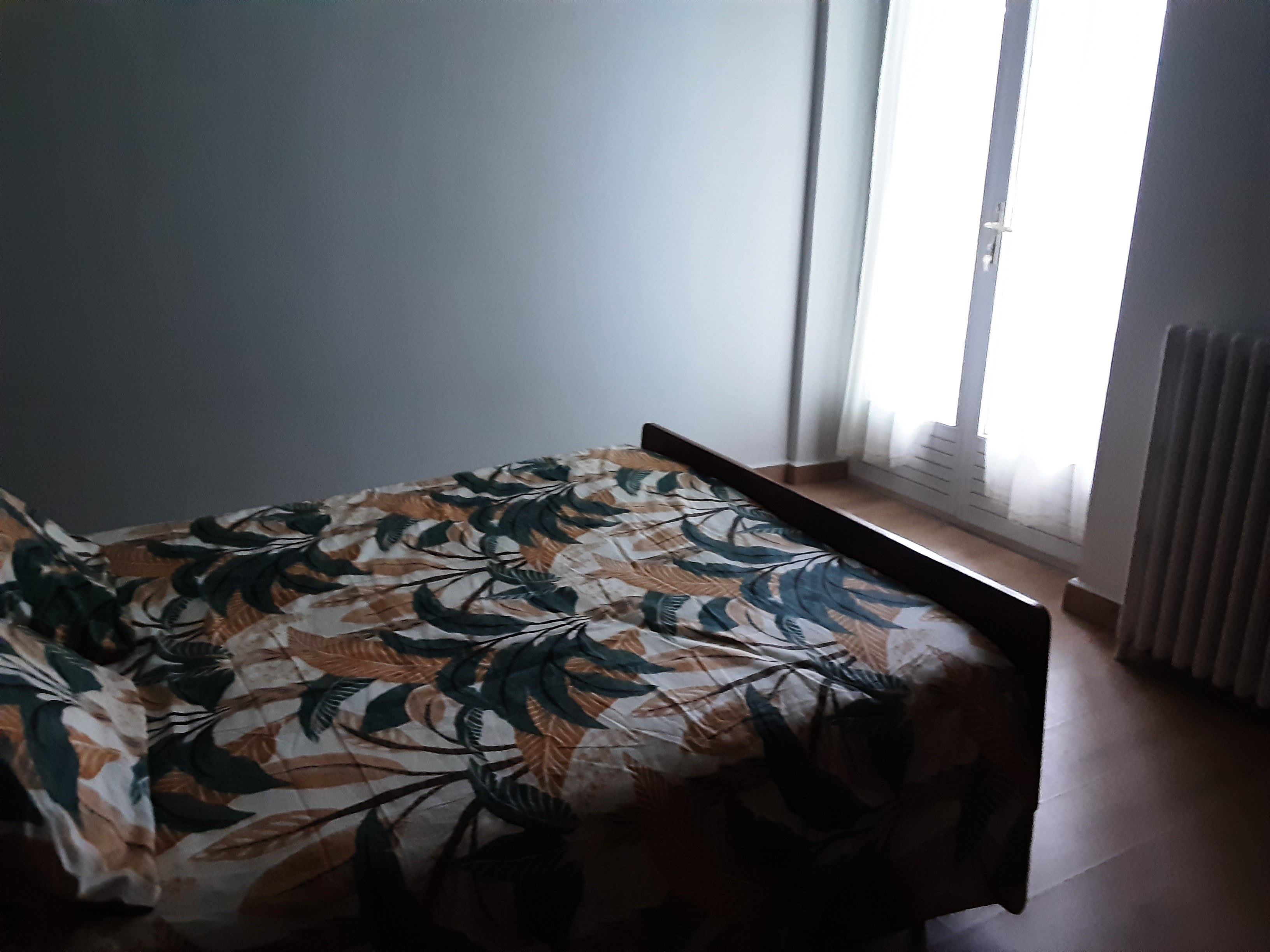 Une chambre à coucher avec un lit, une fenêtre avec des stores et un radiateur.
