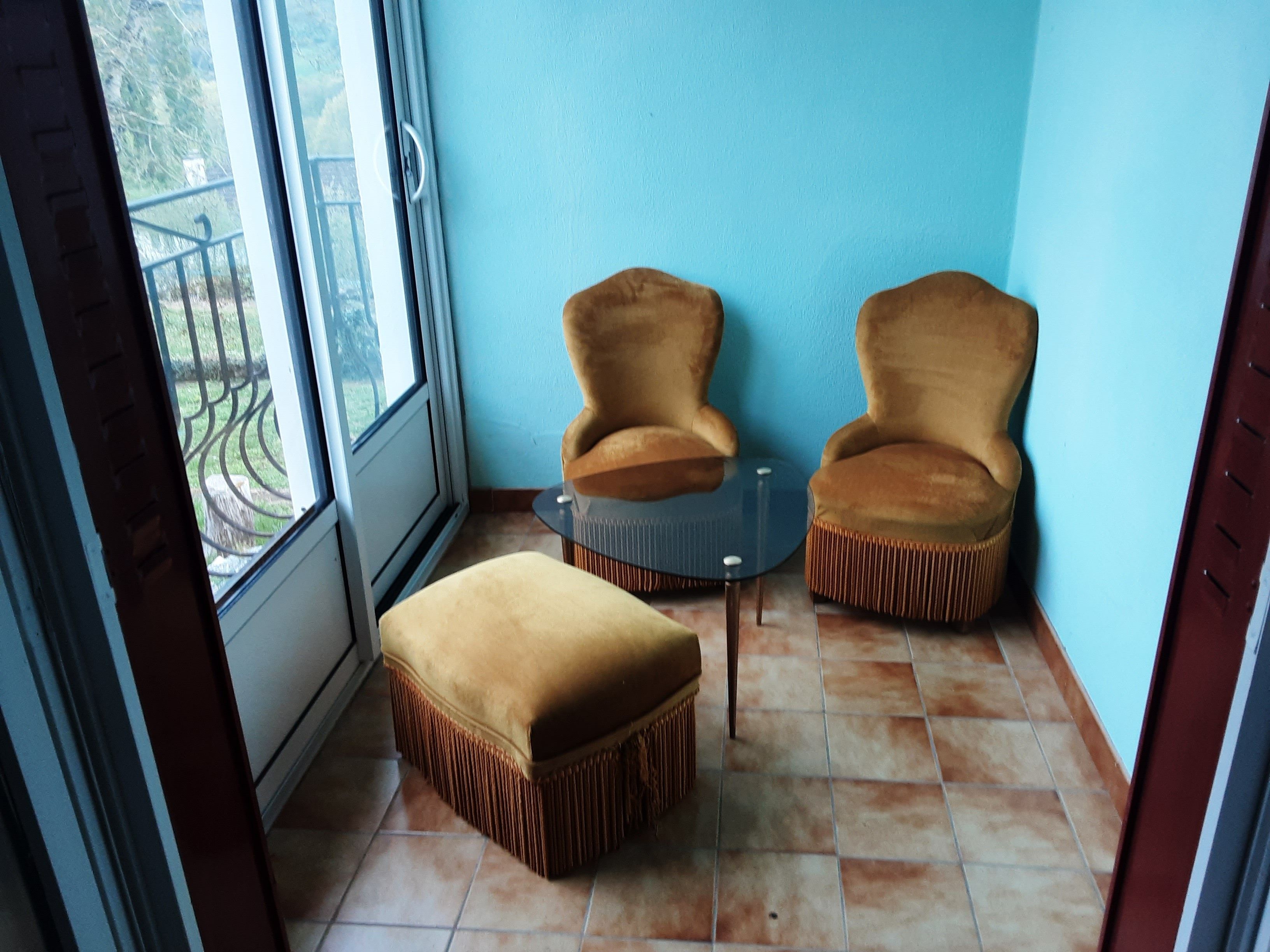 Een kamer met een blauwe wand, een glazen deur naar een balkon, twee fauteuils, een kleine tafel en een bijpassend pouf.