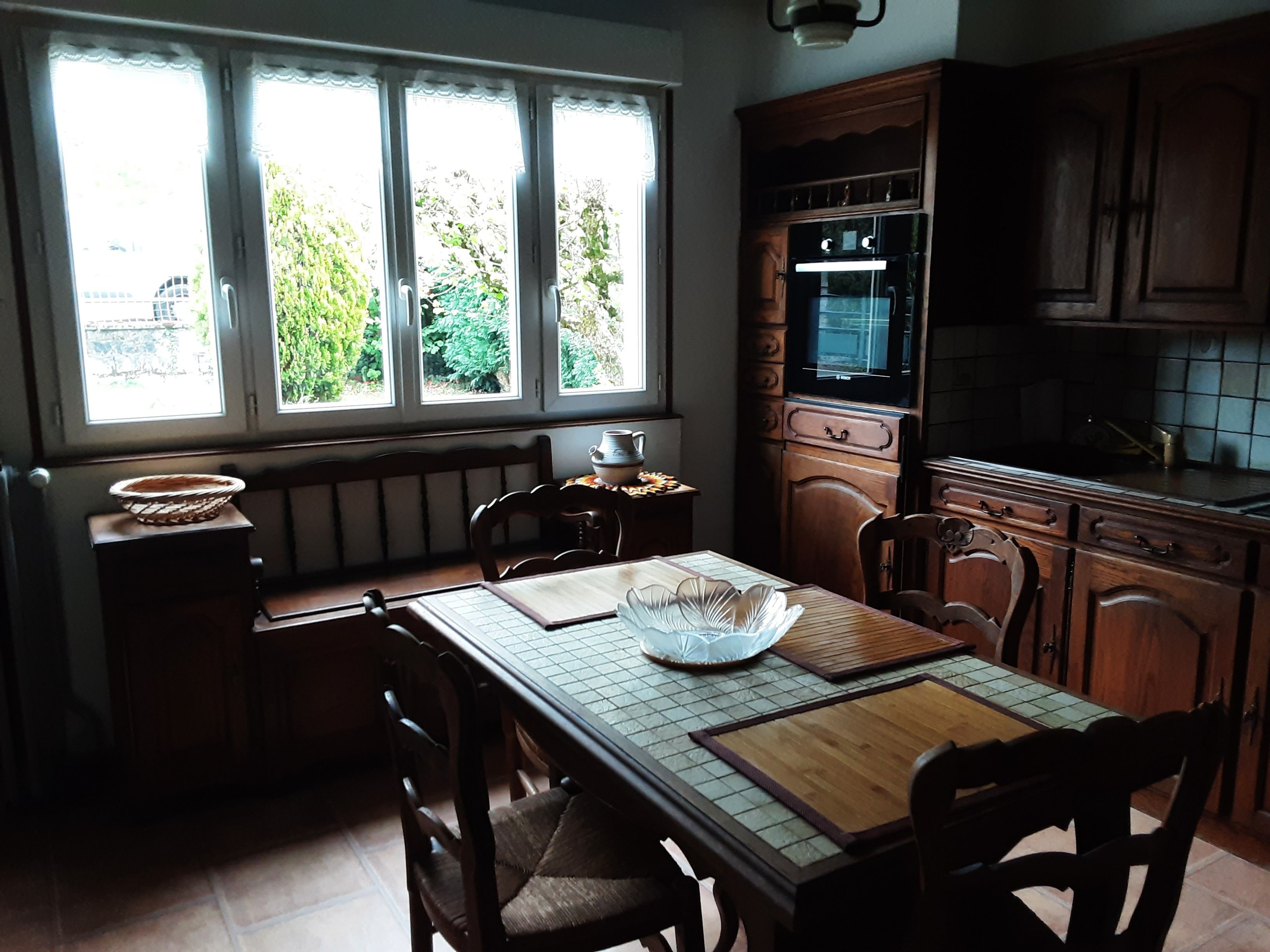 A kitchen with a dining table, chairs, a window with a view of greenery, and wooden cabinets.
