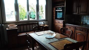 A kitchen with a dining table, chairs, a window with a view of greenery, and wooden cabinets.