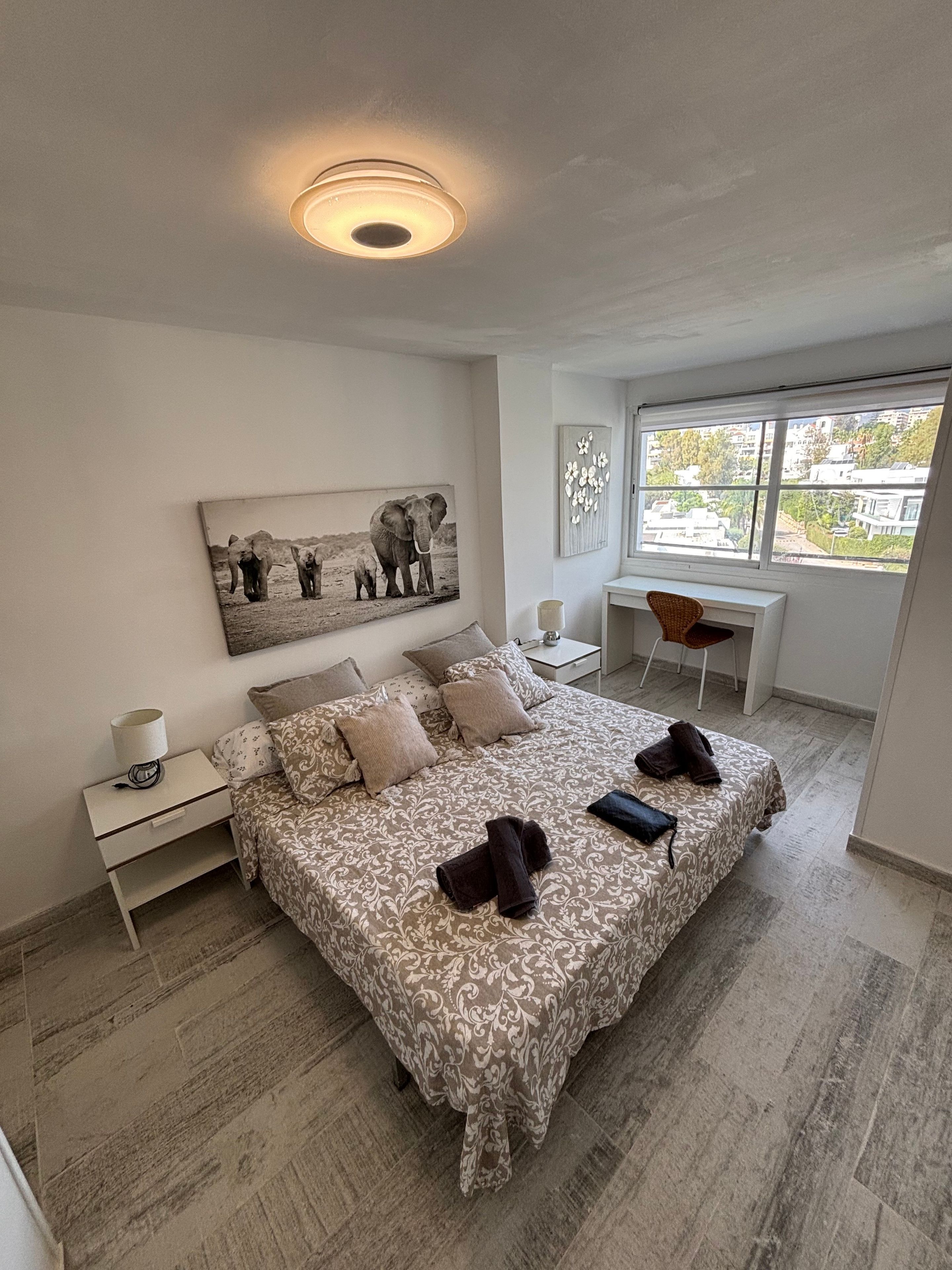 Ein Schlafzimmer mit Bett, Schreibtisch, Stuhl, Nachttisch, Lampe und einem Bild an der Wand.