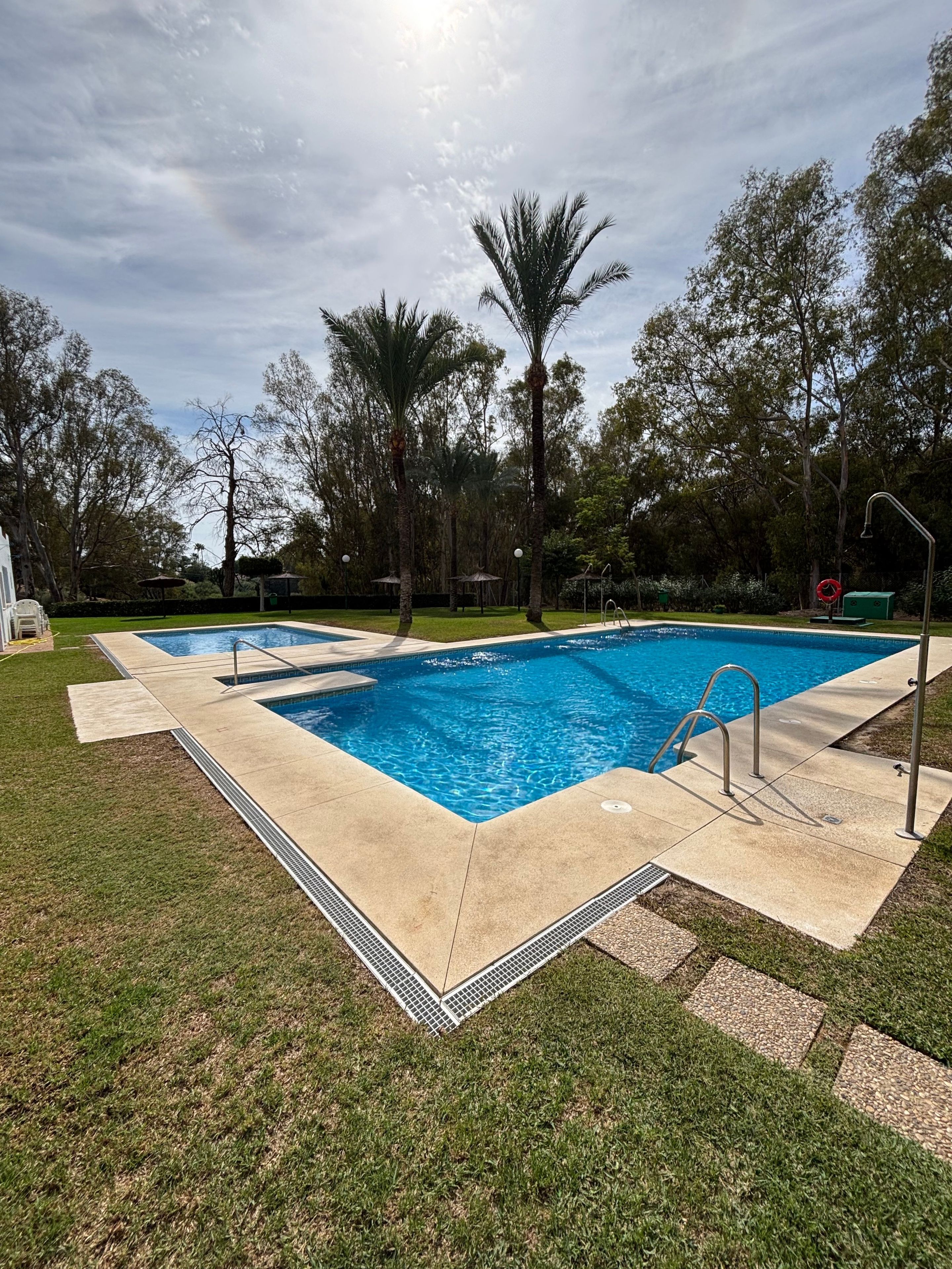 Ein rechteckiger Swimmingpool mit glasklarer, blauer Wasseroberfläche, umgeben von einer Betonplattform und einer Rasenfläche.