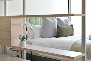 A bed with a headboard, pillows, and a bedside table with a plant. - Stylish 1-Bed Apartment Iconic High-Rise City Views (Cape Town)