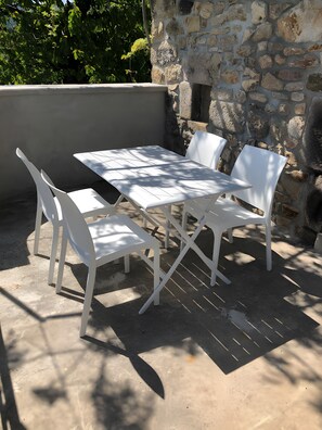 A white outdoor table and chairs set against a stone wall, with shadows cast on the ground. - Holiday Home 'Gîte Chez Zephirin' with Mountain View, Shared Terrace and Wi-Fi (Fabras)