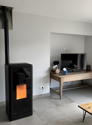 A modern living room with a black wood-burning stove, a television, and a wooden table with a basket and a tissue box. - Holiday Home 'Gîte Chez Zephirin' with Mountain View, Shared Terrace and Wi-Fi (Fabras)