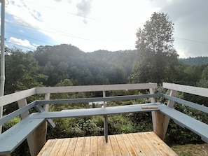 Eine Holzterrasse mit weißer Brüstung mit Blick auf einen bewaldeten Hang.