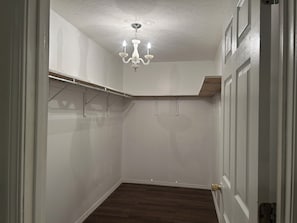 Ein begehbarer Kleiderschrank mit einer Chandelieber, Holzboden und weißen Wänden.