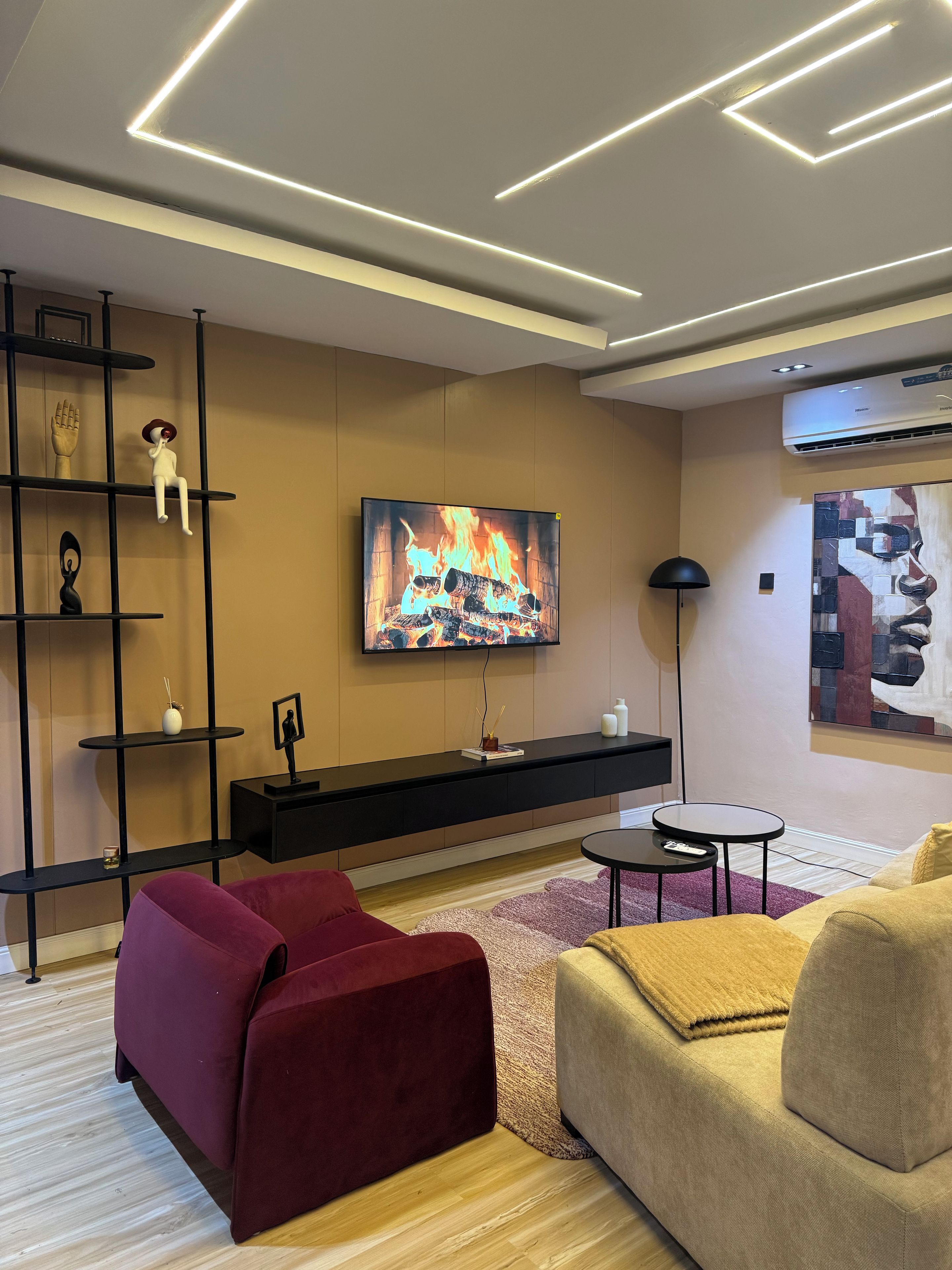 Ein modernes Wohnzimmer mit einem an der Wand befestigten Flachbildfernseher, einer schwarzen Unterhaltungseinheit, einem roten Sofa, einem beigefarbenen Sessel und einem kleinen runden Tisch.