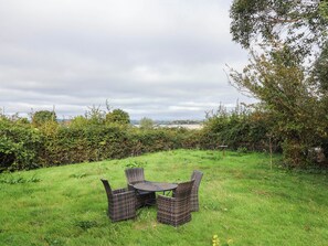 An outdoor seating area with wicker furniture and a table, surrounded by lush greenery and a view of the countryside. - Herriotts Bridge Cottage (Bristol)