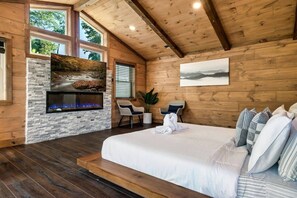 A bedroom with a large bed, a fireplace, a window, and a painting on the wall. - HotTub/FirePit/GameRoom/Theater/VIEWS/Sleeps10! (Gatlinburg)