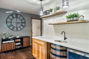 A modern kitchen with a large wall clock, wooden cabinets, a marble countertop, and a built-in wine rack. - HotTub/FirePit/GameRoom/Theater/VIEWS/Sleeps10! (Gatlinburg)