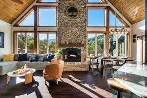A spacious living room with a stone fireplace, large windows, and a high ceiling. - HotTub/FirePit/GameRoom/Theater/VIEWS/Sleeps10! (Gatlinburg)