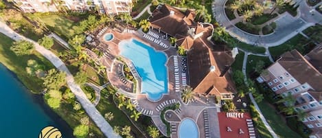 An aerial view of a resort with multiple swimming pools, a central circular pool, and a red-roofed area.