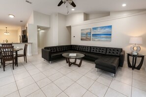 A modern living room with a sectional sofa, a round coffee table, and a dining area with a table and chairs. - Private Pool Villa, 10 Mins to Disney&attractions! (Kissimmee)