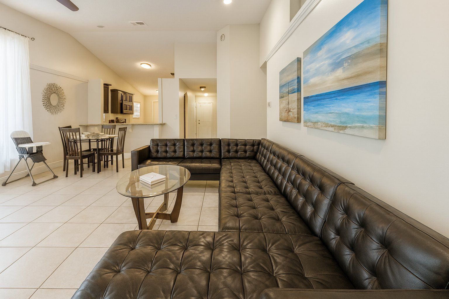 A modern living room with a leather sectional sofa, a glass coffee table, and a dining area with chairs and a table.