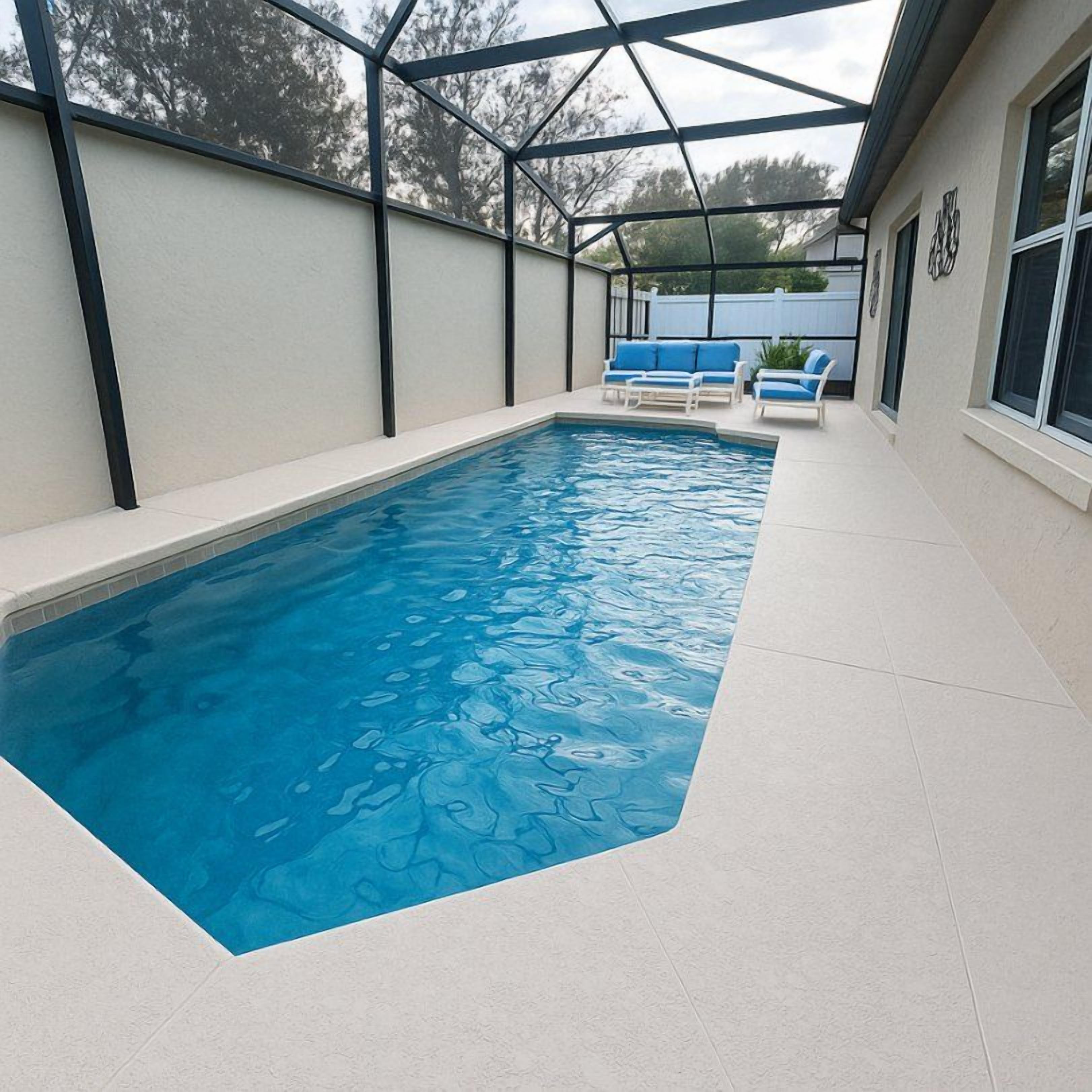 A swimming pool with a glass enclosure, surrounded by a white tiled deck and blue lounge chairs.