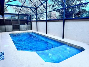 A rectangular indoor swimming pool with clear blue water, surrounded by a white wall and a metal frame structure. - Prime Location! Cozy Villa Near Disney & More (Kissimmee)