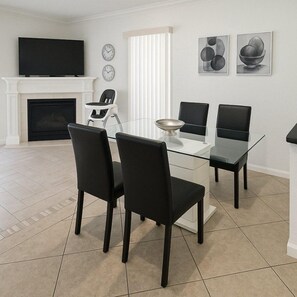 A modern living room with a glass dining table, black chairs, a fireplace, a television, and abstract art on the wall. - Prime Location! Cozy Villa Near Disney & More (Kissimmee)