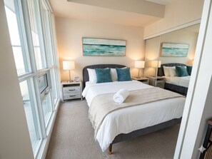 A hotel room with a large bed, two bedside tables, a window, and artwork on the walls. - Toronto Views | 2BR | Raptors - Jays - CN Tower (Toronto)