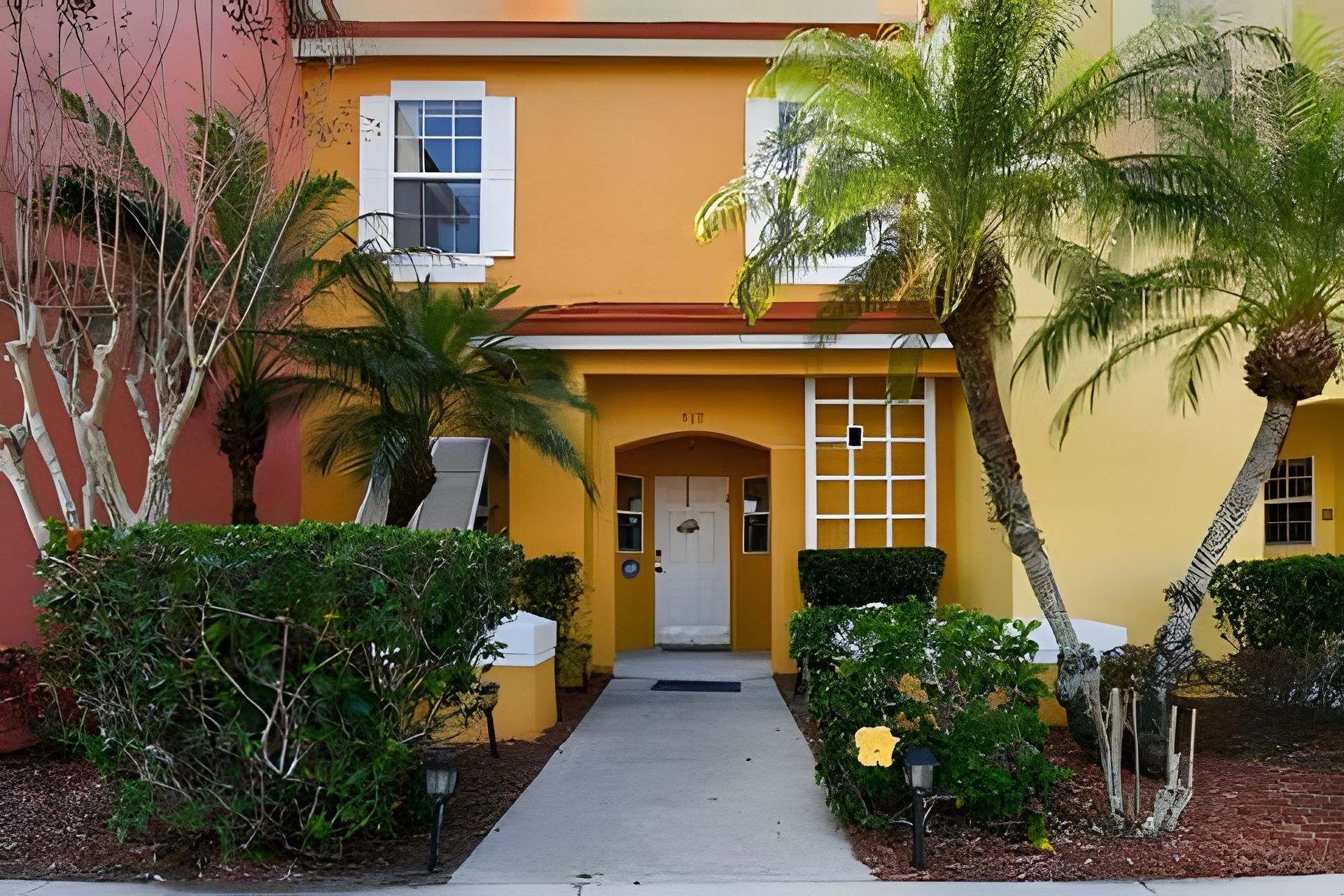 A yellow building with a white door, a small porch, and a pathway leading to the entrance.
