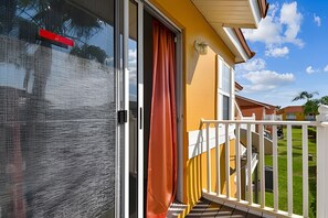 A balcony with a glass door, a white railing, and a yellow wall. - 3BR Lake Berkley Pool Home Near Disney (Kissimmee)