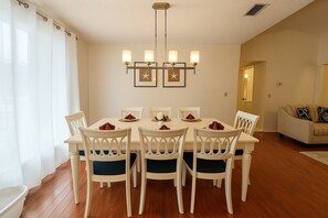 A dining area with a white table and chairs, a chandelier, and framed star decorations on the wall. - Indian Wells 3BR Home w/ Pool 10 min to Disney (Kissimmee)