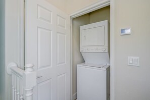 A laundry room with a washer and dryer, a door with a white handle, and a thermostat on the wall. - 3BR Home w/ Private Pool at Serenity (Clermont)