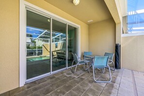 A covered patio with a sliding glass door, outdoor seating, and a view of a swimming pool. - 3BR Home w/ Private Pool at Serenity (Clermont)