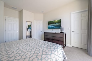 A bedroom with a bed, a dresser, a TV, and two doors. - 3BR Home w/ Private Pool at Serenity (Clermont)
