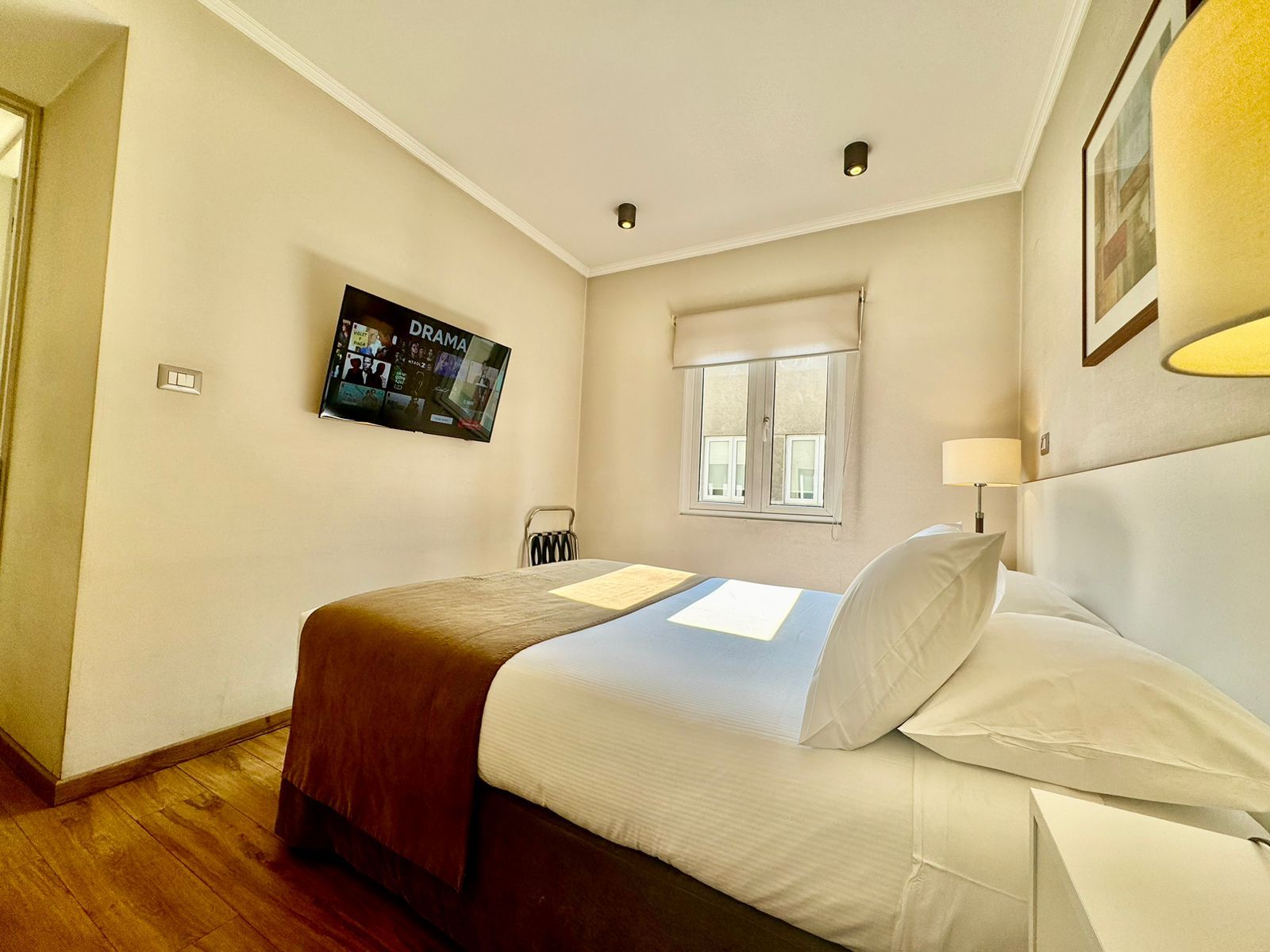 A hotel room with a bed, a television mounted on the wall, a window with a view, and a chair.