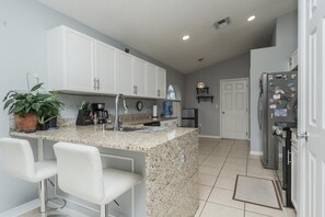 A kitchen with white cabinets, a granite countertop, a sink, a coffee maker, and a refrigerator. - 3BR Pool Home Near Disney in Kissimmee (Kissimmee)