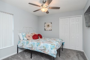 A bedroom with a bed, a ceiling fan, a wall-mounted flower decoration, and a white door. - 3BR Pool Home Near Disney in Kissimmee (Kissimmee)