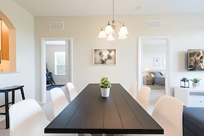 A modern dining area with a dark wooden table, white chairs, a potted plant, and a chandelier. - Vista Cay 3BR Condo Near Universal & Occc (Orlando)